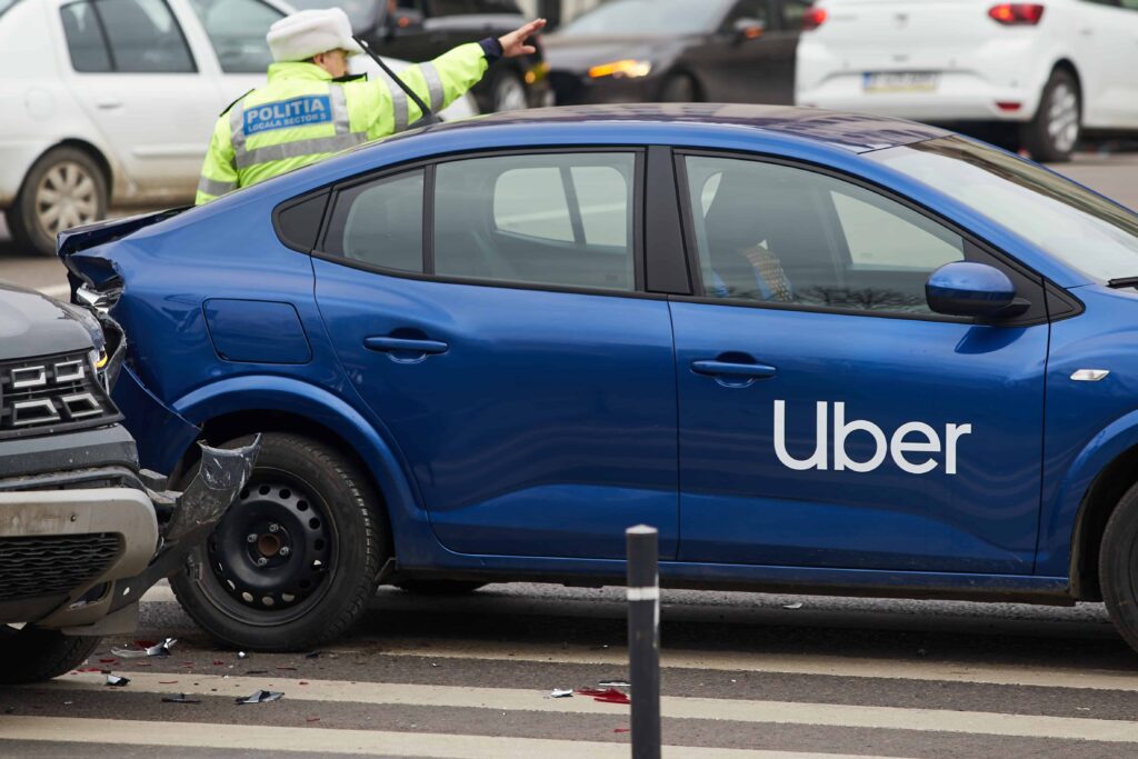 Blue Uber vehicle involved in rear-end car accident with police officer directing traffic at the scene.